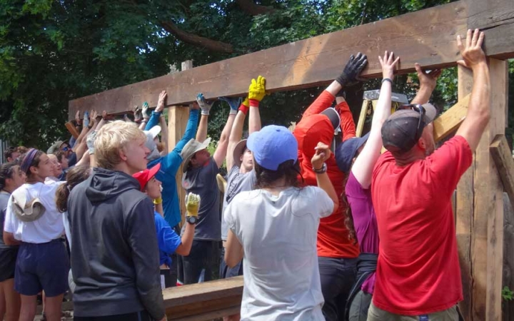 A group of people raise a long piece of wood during a service project. 